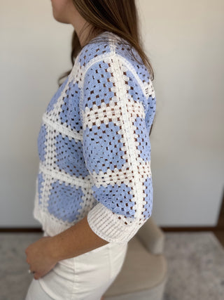 Woman wearing a blue and white crocheted sweater in an indoor setting