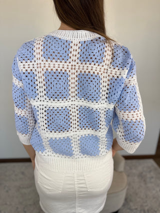 Person wearing a blue and white checkered crochet sweater in a neutral setting