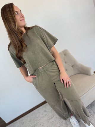 Woman wearing a green outfit standing in a room with a beige sofa.