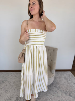 Woman wearing a white and gold striped dress holding a beige handbag indoors.