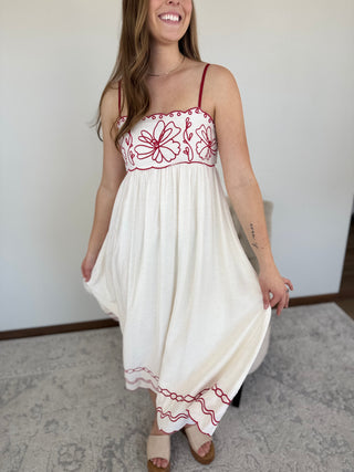 Woman wearing a white dress with red embroidery in a room.