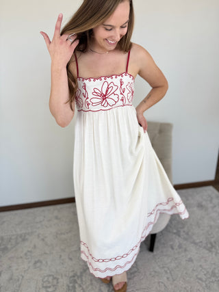 Woman wearing a white dress with red embroidery in a room.