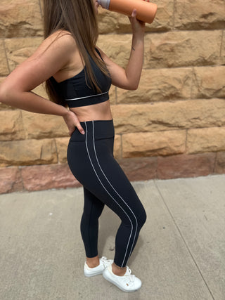 Person wearing black athletic outfit with white stripes, standing against a stone wall.