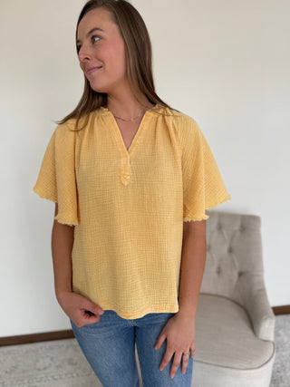 Woman wearing a yellow blouse and blue jeans standing in a room with a gray chair.