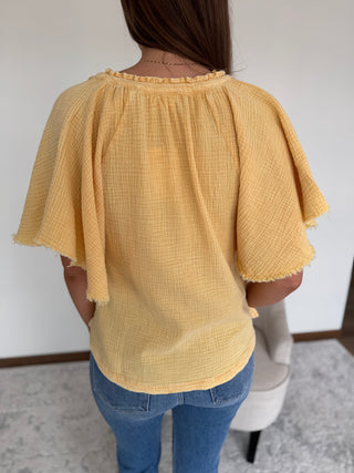 Person wearing a yellow textured blouse and blue jeans against a white wall.