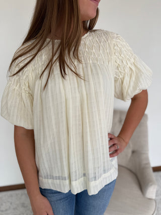 Woman wearing a white blouse with ruffled sleeves and blue jeans indoors.
