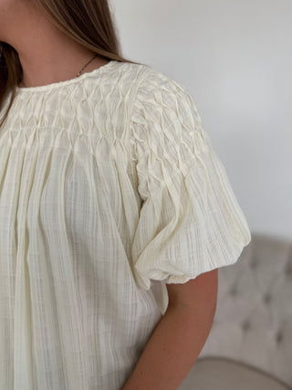Close-up of a person wearing a white textured dress with short sleeves against a neutral background.