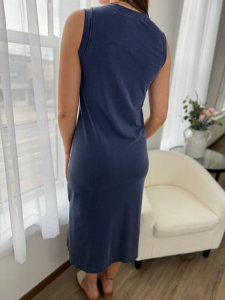 Person wearing a navy blue dress standing in a room with white curtains and a white chair.