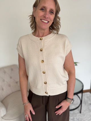 Woman wearing a button up sweater with cap sleeve in taupe.