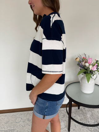 Person wearing a navy and white striped shirt with denim shorts in a room with a table and flowers.