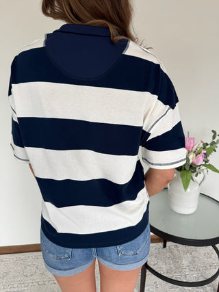Person wearing a navy and white striped shirt with denim shorts, standing indoors.