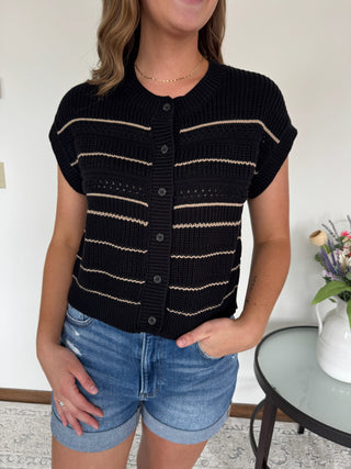 Person wearing a black and white striped short-sleeve cardigan with denim shorts indoors.