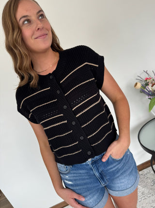 Woman wearing a black striped vest and denim shorts indoors.