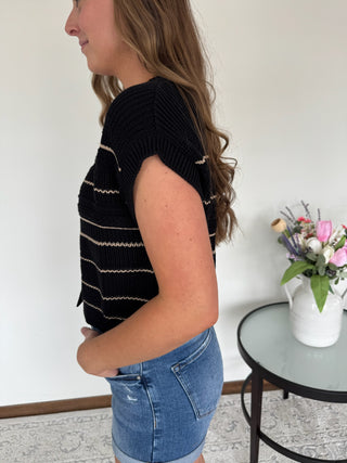 Woman wearing a black striped vest and denim shorts indoors.