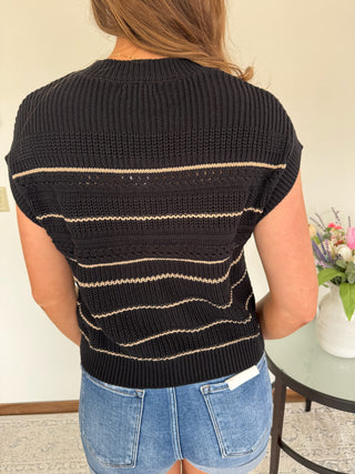 Person wearing a black and beige striped sleeveless sweater with a blurred background