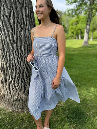 Woman in a blue striped dress standing next to a tree in a park