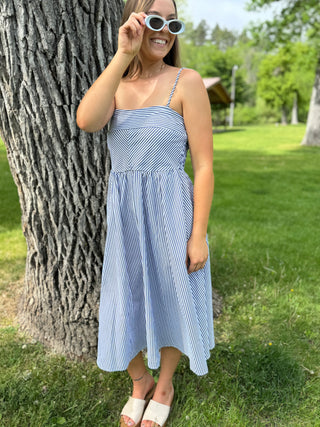 Woman in a blue striped dress standing next to a tree in a park
