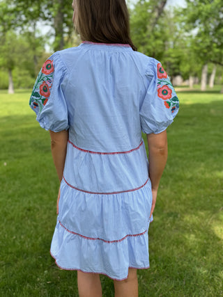 Person wearing a light blue dress with floral sleeves in an outdoor setting