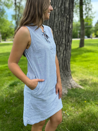 Woman wearing a light blue dress standing in a park with trees and grass in the background