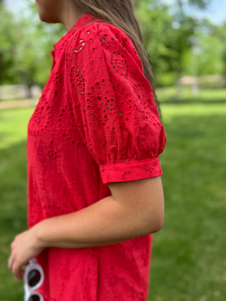 Person wearing a red lace dress with a blurred green outdoor background