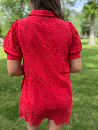 Person wearing a red lace dress standing in a grassy area with trees in the background