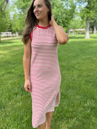 Woman wearing a red and white striped dress standing in a grassy area with trees in the background