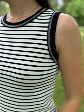 Person wearing a black and white striped sleeveless top with a blurred green background