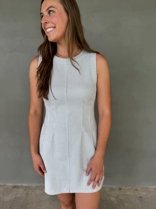 Woman wearing a light blue sleeveless dress against a gray wall.