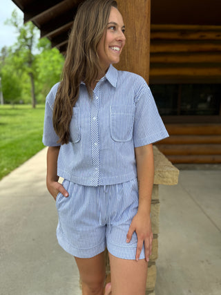 Woman wearing a blue and white striped shirt and shorts set standing outdoors.