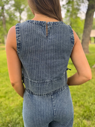 Person wearing a blue denim jumpsuit standing in a grassy area with trees.