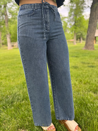 Person wearing blue striped jeans standing in a grassy area with trees in the background