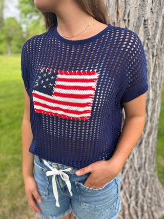 Person wearing a navy blue knit top with an American flag patch outdoors.