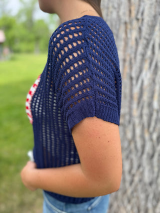 Person wearing a blue knit top with a blurred outdoor background