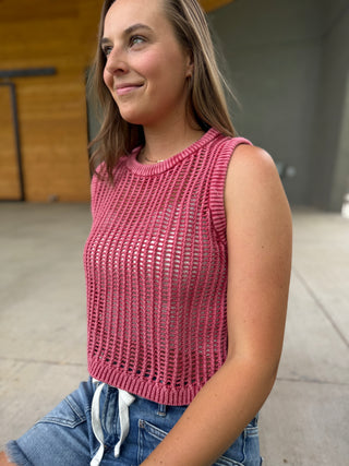 Woman wearing a pink sleeveless knitted top and blue jeans outdoors.