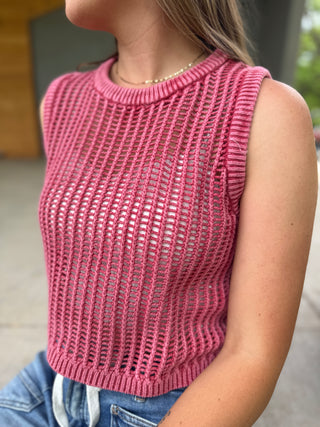 Person wearing a pink knitted sleeveless top with a blurred background