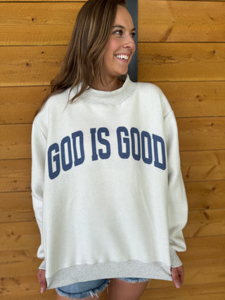 Woman wearing a white sweatshirt with 'GOD IS GOOD' text against a wooden background