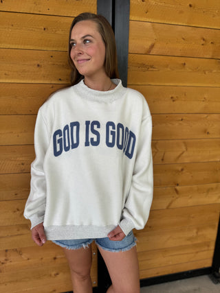 Woman wearing a 'GOD IS GOOD' sweatshirt against a wooden wall