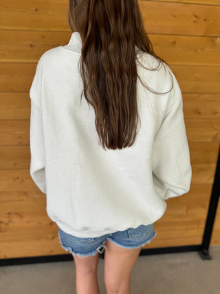 Person wearing a white oversized shirt and denim shorts standing against a wooden wall.