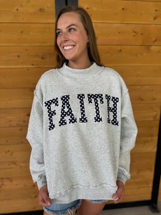 Woman wearing a gray sweatshirt with 'FAITH' printed on it in front of a wooden wall.