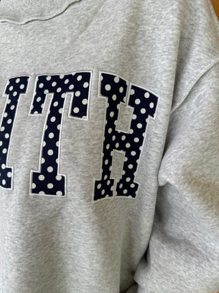 Gray sweatshirt with navy polka dot letters on a wooden surface