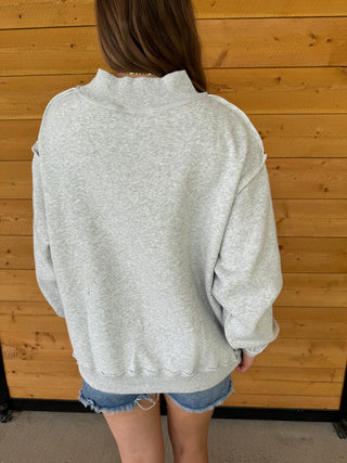 Person wearing a gray sweatshirt and denim shorts standing against a wooden wall.