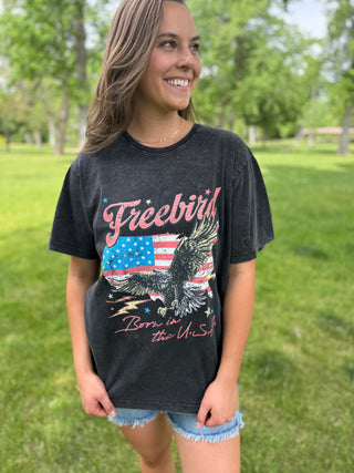 Woman wearing a black t-shirt with an eagle and American flag design, standing in a park.