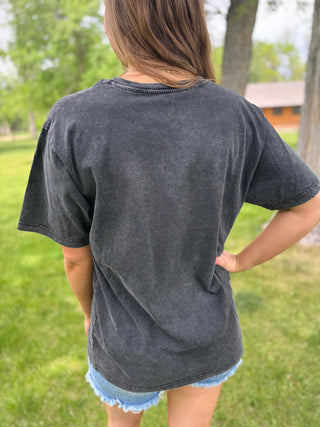 Person wearing a dark gray t-shirt in an outdoor setting with green grass and trees.