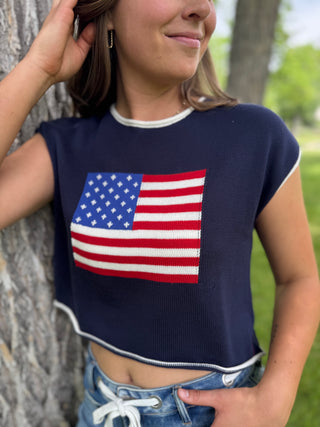 Person wearing a navy blue crop top with an American flag design, standing outdoors.