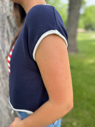 Person wearing a navy blue sleeveless top with white trim in an outdoor setting