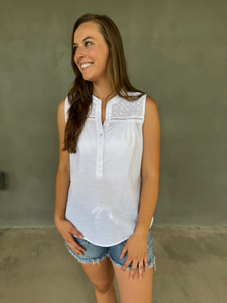 Woman wearing a white sleeveless top with lace details and denim shorts against a plain background