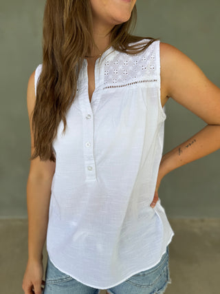 Woman wearing a white sleeveless blouse with lace details against a neutral background