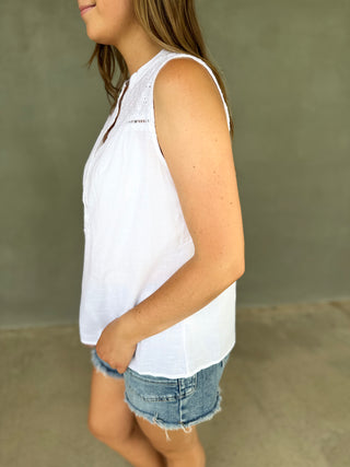 Person wearing a white sleeveless top and denim shorts against a neutral background