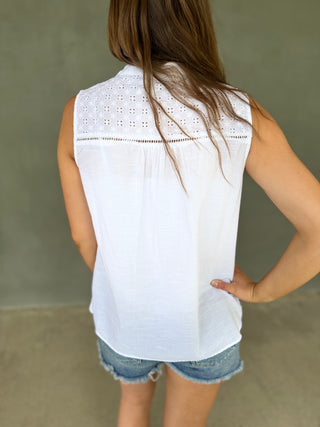 Person wearing a white sleeveless top with lace details and denim shorts against a neutral background