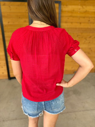 Person wearing a red checkered shirt and denim shorts standing against a wooden wall.